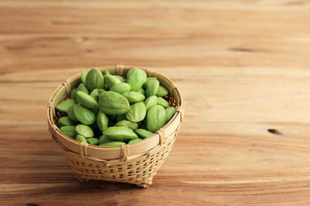 Bitter Bean, Twisted Cluster Bean, Stinky Bean, Sato, Petai or Parkia speciosa. Cooking in a Bamboo Basket Bowl Isolate on Wooden Tableの写真素材