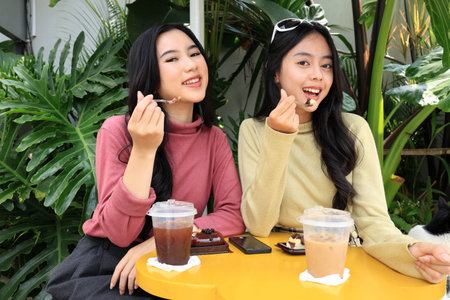 Two Young Asian Girl Eating Dessert while Looking at Camera in an Outdoor Coffee Shopの写真素材