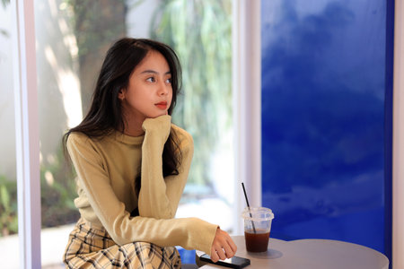 Young Asian Female  Teenager Sitting at Cozy Cafe with A Cup of Americanoの写真素材