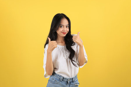 Young Asian Teenager  Women Happy  Smiling to the Camera and Give Two Thumbs Up, Isolated on Yellow Backgroundの写真素材