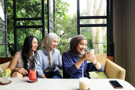 Three Asian Female Friends Hanging Out at cafe restaurant, Looking at Mobile Phone, Laughing at...