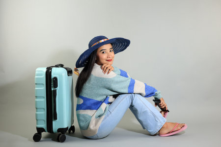 Young Asian Woman Leaning on Standing Suitcase, Looking at Camera Excited to Go on Summer Vacation, Isolated on Grey Backgorund, Copy Space for Textの写真素材