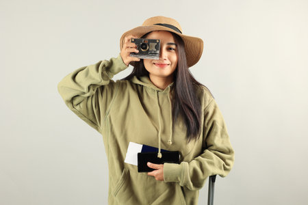 Happy Asian Woman Traveler with Luggage, Camera, Passport, Boarding Pass Ticket,  and  Mobile Phone Isolated on Grey Background. Indonesian Female Happy Trip Conceptの写真素材