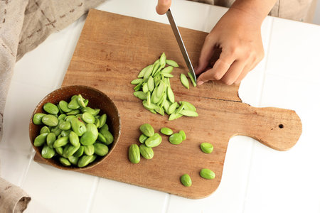 Top View Female Hand Cutting and Slicing Fresh Peeled Petai on Wooden Cutting Board