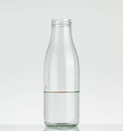 Glass bottle half filled with water. Water bottle without cap isolated on white background.の写真素材