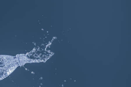 Splash of water from a bottle on a blue background. Reflection on the surface of the water.の写真素材