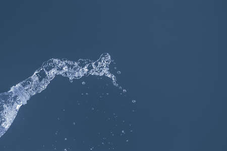 Splash of water from a bottle on a blue background. Reflection on the surface of the water.の写真素材