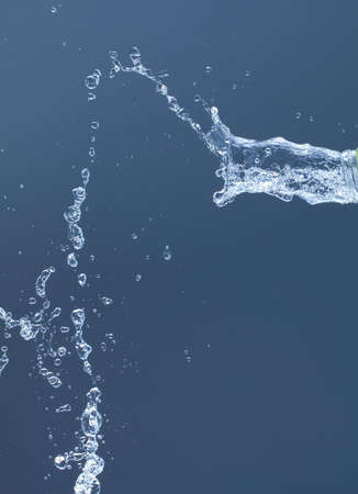 Splash of water from a bottle on a blue background. Reflection on the surface of the water.の写真素材