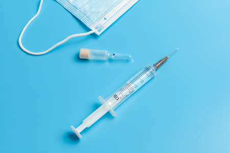 Medical mask, syringe and ampoule. A blue medical mask with a white elastic band, a syringe and an...