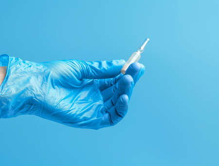 Medical glove. An ampoule with a white liquid in his hand in a blue medical glove. Isolated on a blue background.の写真素材