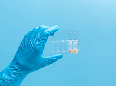 Medical glove. Ampoules with a white liquid in the hand in a blue medical glove. Isolated on a blue background.の写真素材