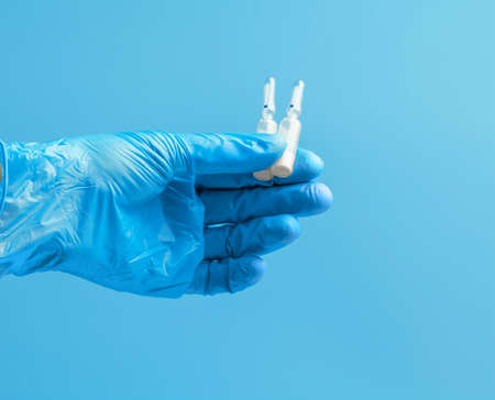 Medical glove. Ampoules with a white liquid in the hand in a blue medical glove. Isolated on a blue background.の写真素材