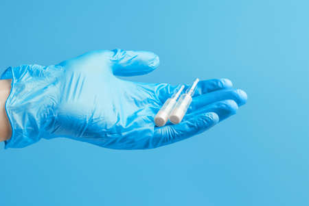 Medical glove. Ampoules with a white liquid in the hand in a blue medical glove. Isolated on a blue background.の写真素材