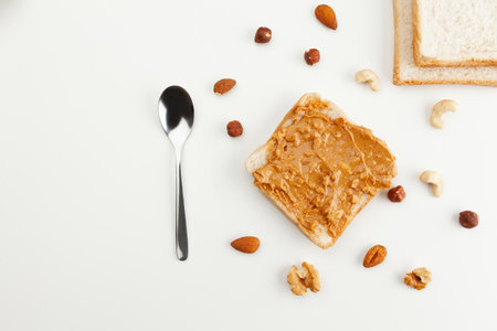 Square bread for toast with peanut butter. Nuts, spoon, bread slices and a peanut butter sandwich on a white table.の写真素材