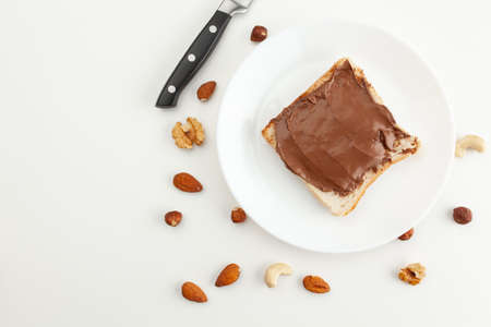 Bread with chocolate paste on a plate. Knife and various types of nuts. Cashew, almond, walnut, hazelnut isolated on white background.の写真素材
