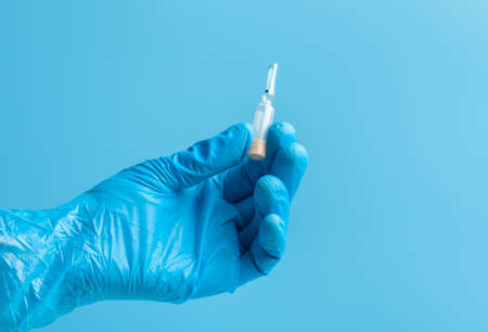 Medical glove. An ampoule with a white liquid in his hand in a blue medical glove. Isolated on a blue background.の写真素材