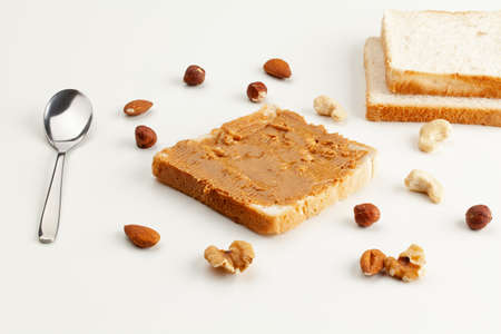 Square bread for toast with peanut butter. Nuts, spoon, bread slices and a peanut butter sandwich on a white table.の写真素材