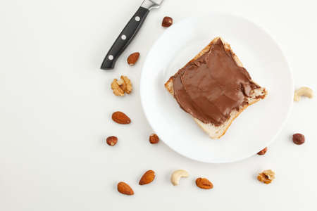 Bread with chocolate paste on a plate. Knife and various types of nuts. Cashew, almond, walnut, hazelnut isolated on white background.の写真素材