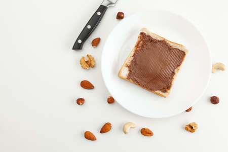 Bread with chocolate paste on a plate. Knife and various types of nuts. Cashew, almond, walnut, hazelnut isolated on white background.の写真素材