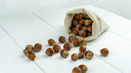 A bunch of hazelnuts in a pouch scattered on a wooden tableの写真素材