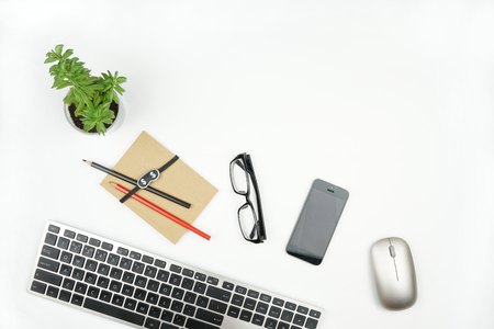 White office table with computer gadgets, flower and notepad with pencils, glasses and phone. Flat lay with copy space.の写真素材