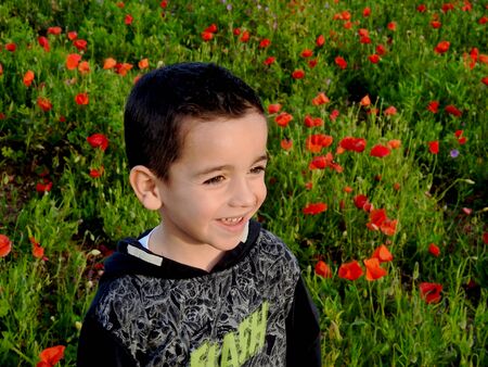 happy boy with a big smile playing in a poppy field on a sunny spring dayの写真素材