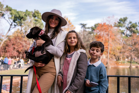 Happy mom in outerwear hugging Labrador Retriever puppy with leash and smiling while standing near...