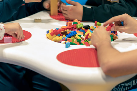 Group of crop children sitting at table and playing with colorful bricks on weekend day in playroomの写真素材