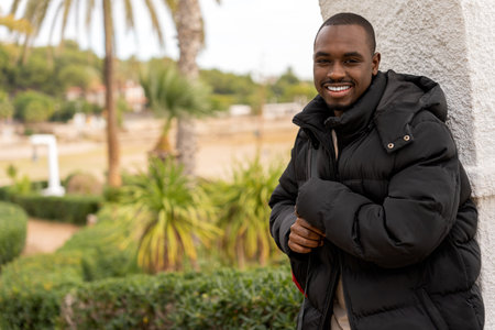 Portrait of smiling African American male in windbreaker jacket looking at camera while standing on...