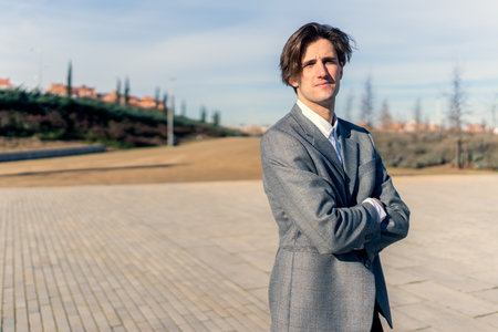 Serious young businessman in formal suit standing with arms crossed and looking at camera against cityscapeの写真素材