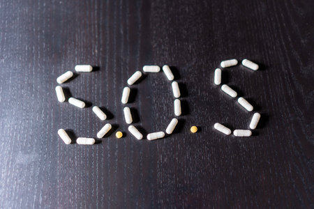 Top view of SOS signal abbreviation made with pills on black wooden table in daylightの写真素材