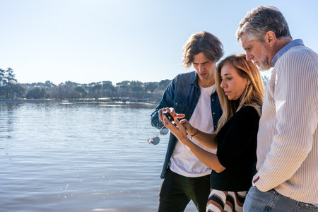 Side view of mature mother with cellphone showing photos while young son pointing at screen and...