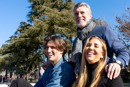 Smiling mature gray haired man putting hands on shoulders of wife and son while standing outside...