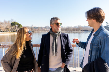 Young man having pleasant conversation with mature mother and father while standing near river in...