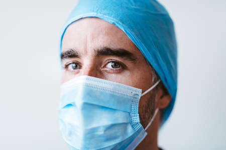 Doctor leaning against a glass window with a tired expression while wearing a mask and uniform.の写真素材
