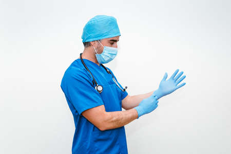 Doctor leaning against a glass window with a tired expression while wearing a mask and uniform.