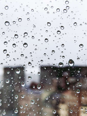 Vertical photo of raindrops on a glass with silhouette of buildings out of focus in the background