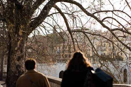 People walking along a tree-lined promenade around a riverの写真素材