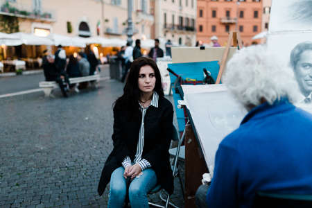 Roma, Italy, November 1, 2015: Older man painting a girl sitting on a chair in a baroque square.のeditorial素材
