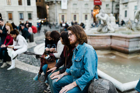 Roma, Italy, November 1, 2015: A group of young tourists sitting at a fountain in a square of a cityのeditorial素材