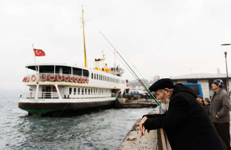 Istanbul, Turkey, December 1, 2014: Fishermen on the harbor promenade next to a ferry on winterのeditorial素材