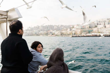 Istanbul, Turkey, December 1, 2014: Family on a ferry boat watching the seagulls flying around with...
