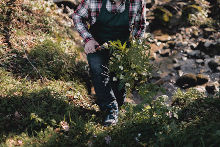 Gardener carrying a bouquet of flowers through the forest with a stream in the backgroundの写真素材