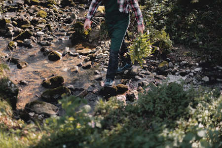 Detail of the legs of a gardener carrying a bouquet of violet flowers as he crosses a streamの写真素材