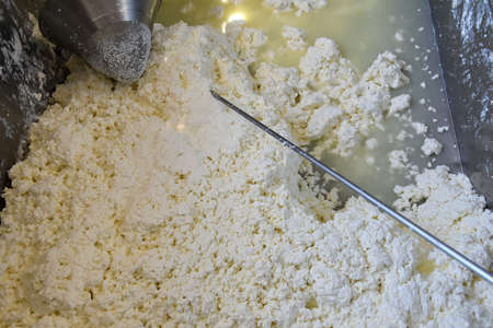Curd of cow and goat milk with a stirrer and a strainer on top, prepared to make cheese.