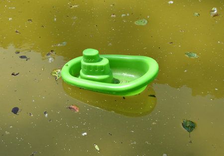 Green toy plastic boat in small pond with green water and plant debris. Pond of the laundry of the village of ArmejÃºn, province of Soria, Spain.の写真素材
