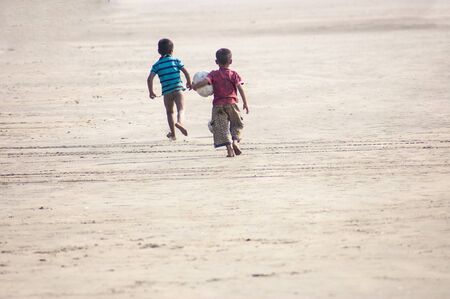 Two boys running joyfully with a ball on a beachの写真素材