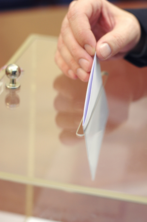 Image of a ballot box and hand putting a blank ballot inside,elections, voting concept.の写真素材