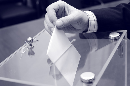 Image of a ballot box and hand putting a blank ballot inside,elections, voting concept