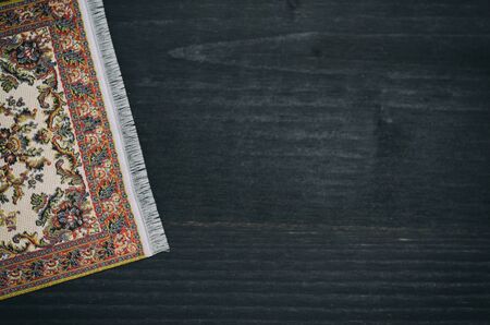 Oriental Persian carpet on black wooden background, decoration concept.